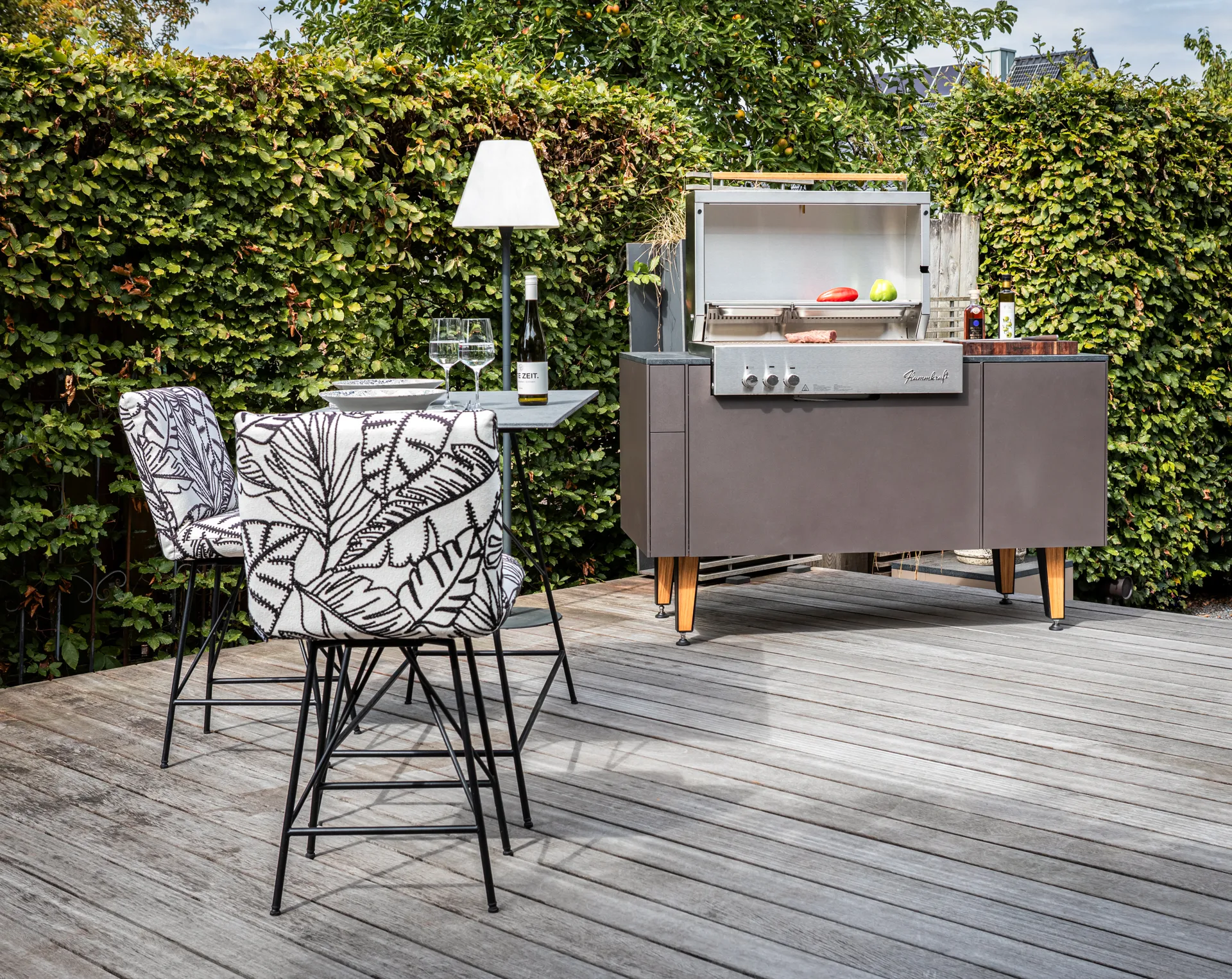 Freiluft Grillmodul auf Holzbeinen neben einem Bartisch auf der Terrasse